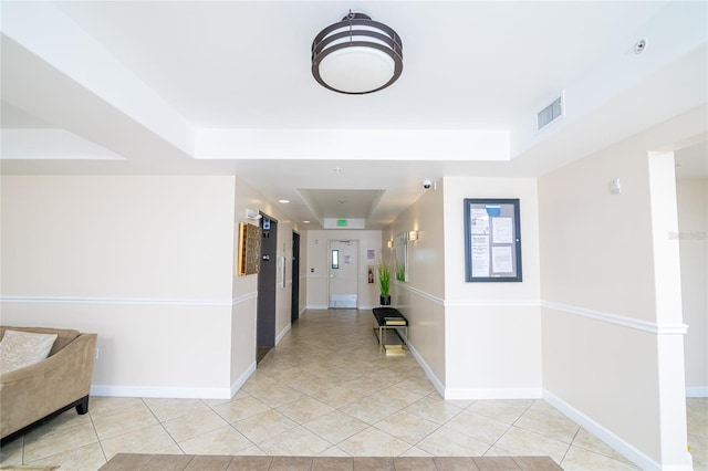 hall with a raised ceiling and light tile patterned floors