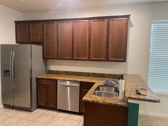 kitchen with dark stone counters, stainless steel appliances, sink, light tile patterned flooring, and dark brown cabinetry