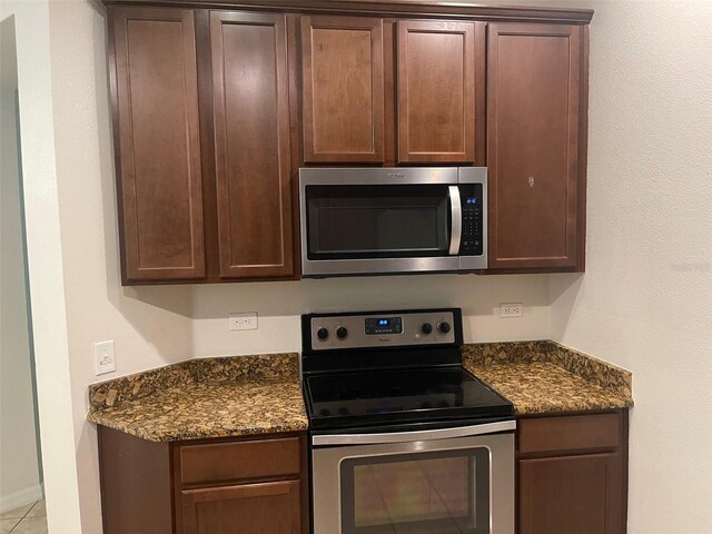 kitchen with stainless steel appliances, dark stone countertops, dark brown cabinetry, and light tile patterned flooring