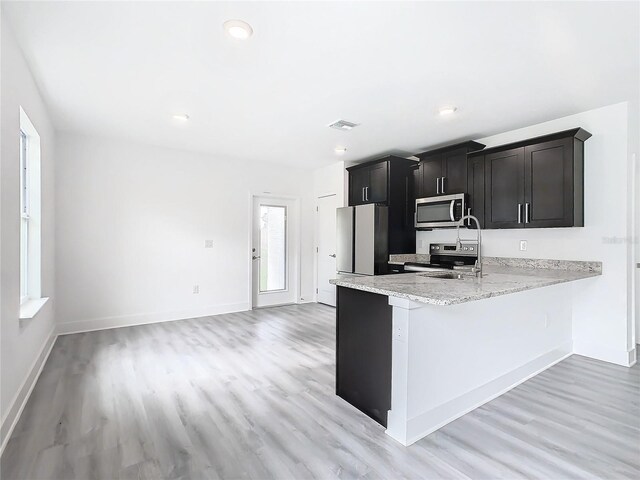 kitchen with light stone counters, stainless steel appliances, kitchen peninsula, and light hardwood / wood-style flooring