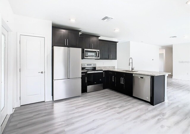 kitchen with stainless steel appliances, sink, light wood-type flooring, and kitchen peninsula