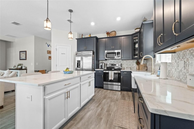 kitchen featuring light stone counters, a kitchen island, decorative light fixtures, appliances with stainless steel finishes, and light wood-type flooring