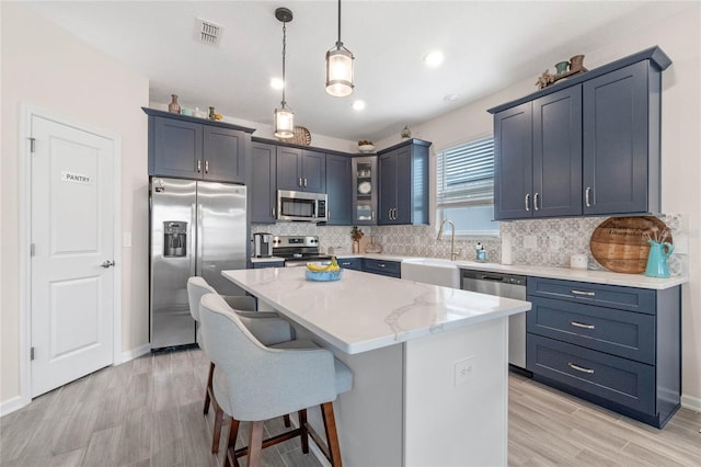 kitchen featuring appliances with stainless steel finishes, light stone counters, pendant lighting, a center island, and sink