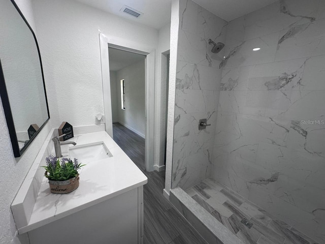 bathroom with wood-type flooring, vanity, and a tile shower