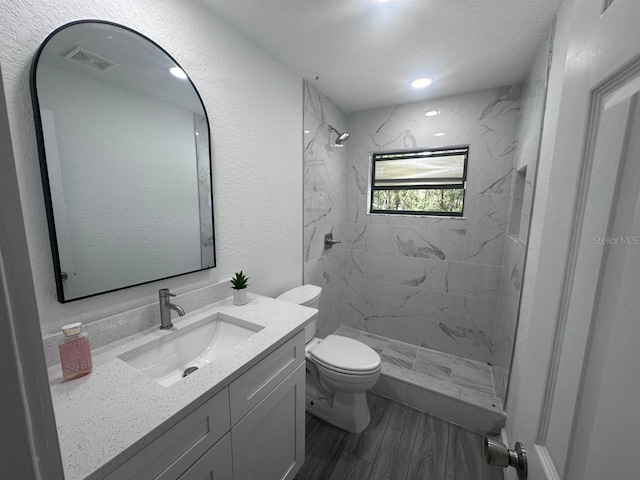 bathroom with tiled shower, vanity, a textured ceiling, and toilet