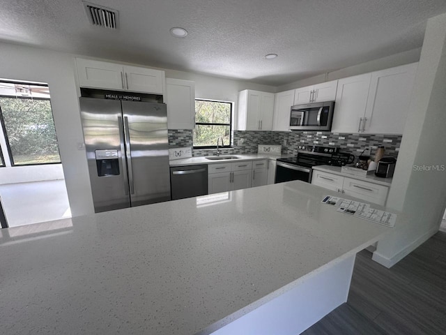 kitchen with light stone counters, sink, tasteful backsplash, white cabinetry, and appliances with stainless steel finishes