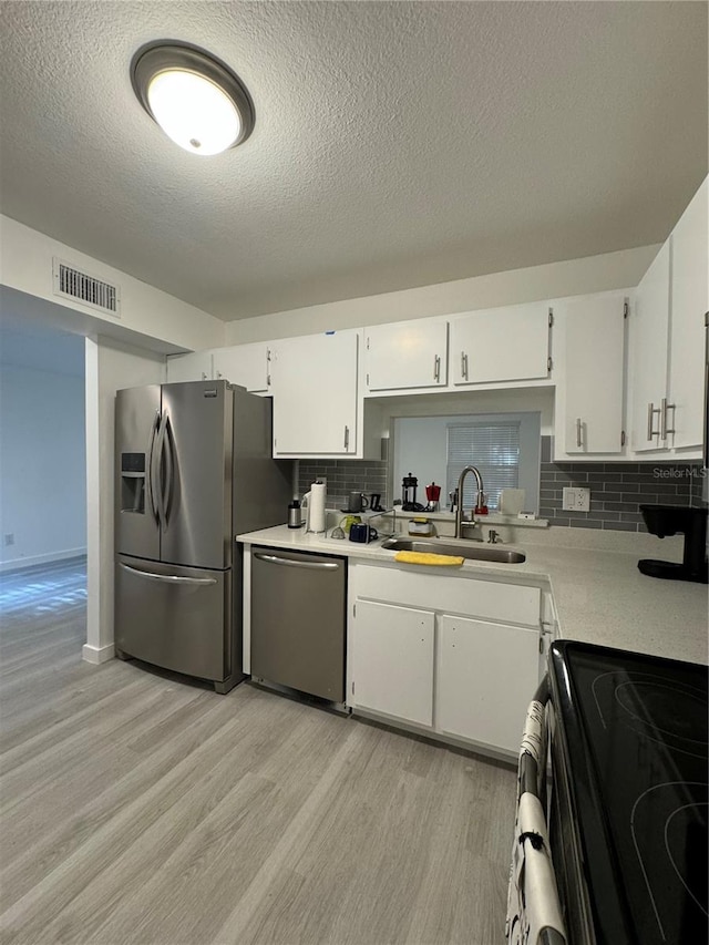 kitchen with light wood-type flooring, backsplash, stainless steel appliances, and white cabinets