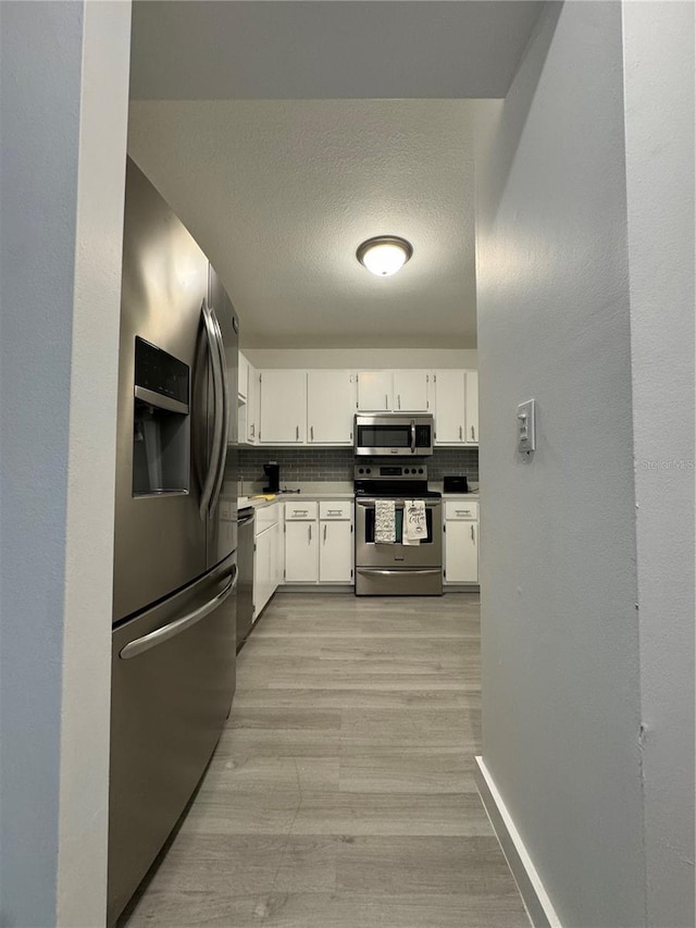 kitchen with a textured ceiling, backsplash, white cabinetry, appliances with stainless steel finishes, and light wood-type flooring