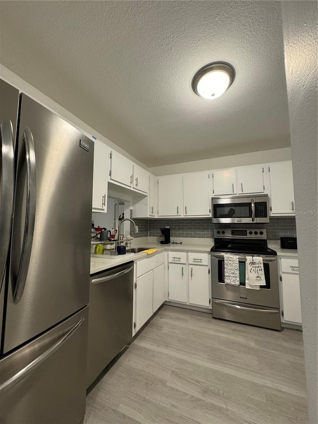 kitchen featuring tasteful backsplash, white cabinets, stainless steel appliances, light wood-type flooring, and a textured ceiling