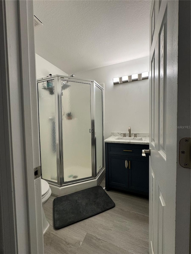 bathroom with vanity, a textured ceiling, wood-type flooring, a shower with door, and toilet