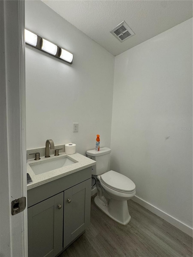 bathroom with a textured ceiling, hardwood / wood-style flooring, vanity, and toilet