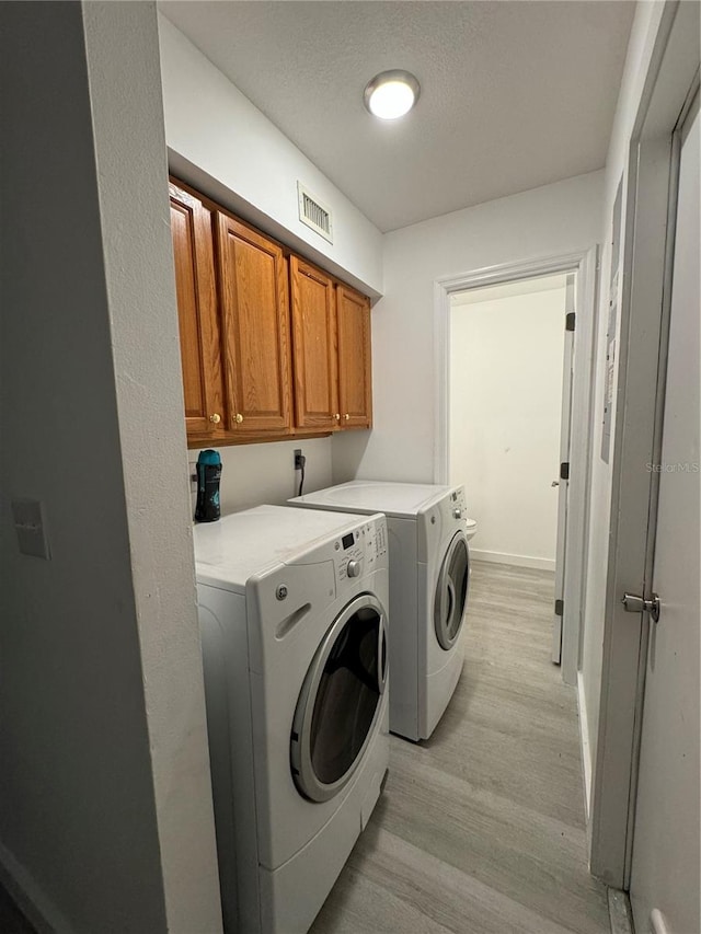 laundry room featuring a textured ceiling, separate washer and dryer, light hardwood / wood-style flooring, and cabinets