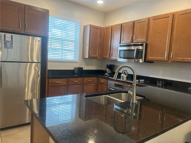 kitchen with appliances with stainless steel finishes, dark stone countertops, sink, and light tile patterned floors