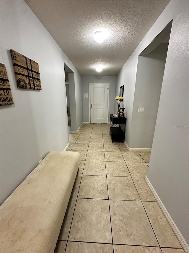 hallway with a textured ceiling and light tile patterned floors