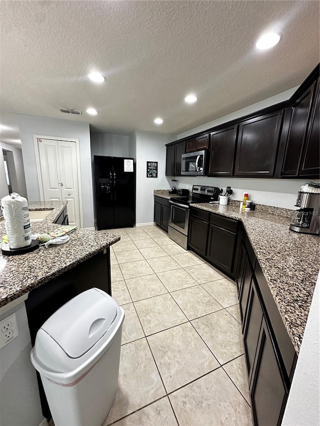 kitchen featuring dark stone countertops, a textured ceiling, stainless steel appliances, and light tile patterned floors