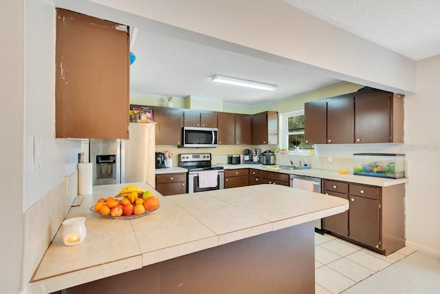 kitchen featuring sink, kitchen peninsula, stainless steel appliances, light tile patterned floors, and dark brown cabinetry