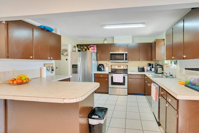 kitchen with light tile patterned floors, sink, stainless steel appliances, and kitchen peninsula