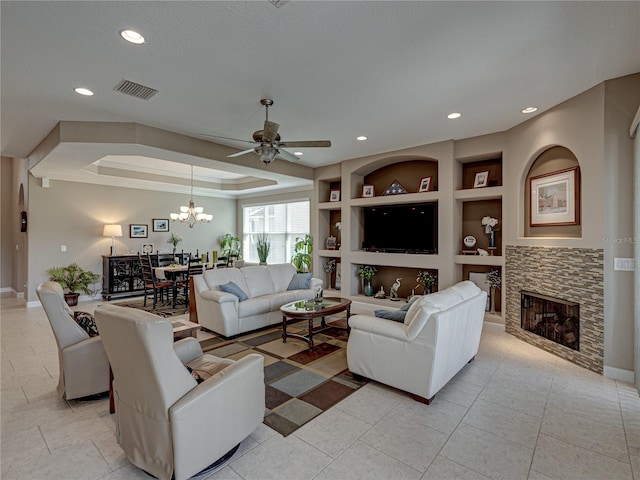 tiled living room featuring built in shelves, a stone fireplace, and ceiling fan with notable chandelier