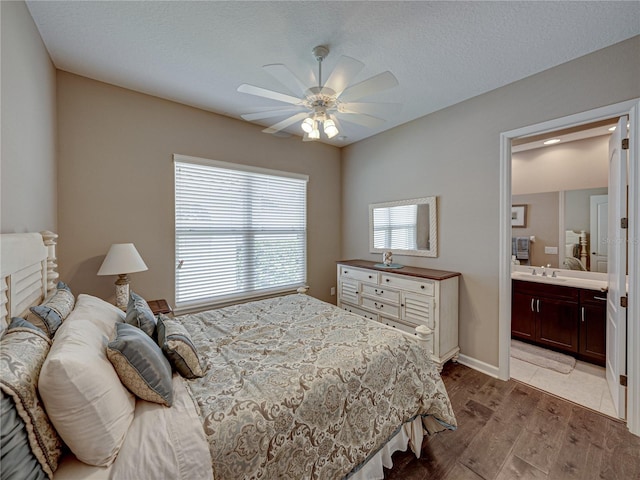 bedroom featuring light hardwood / wood-style floors, a textured ceiling, ceiling fan, ensuite bathroom, and sink