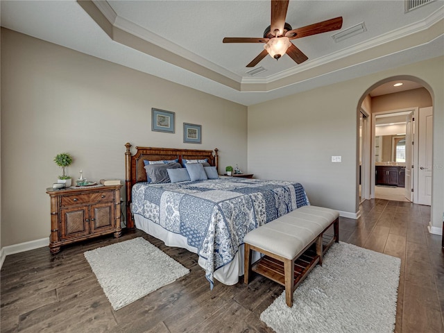 bedroom with ceiling fan, connected bathroom, ornamental molding, a tray ceiling, and dark hardwood / wood-style flooring