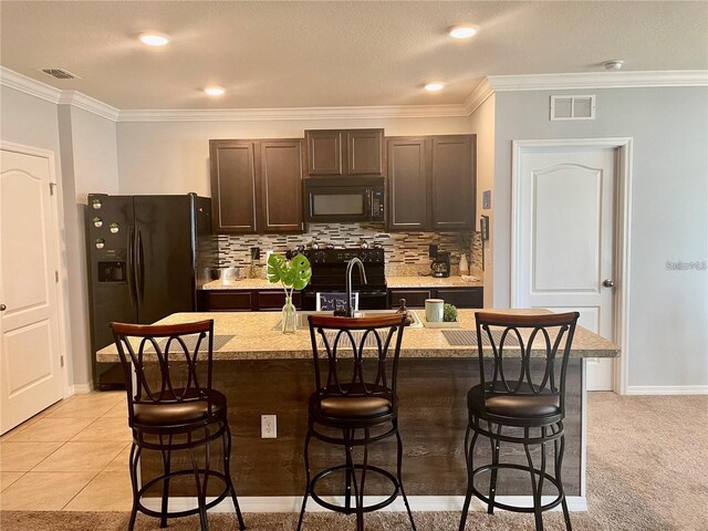 kitchen with a kitchen breakfast bar, dark brown cabinets, black appliances, and a kitchen island with sink