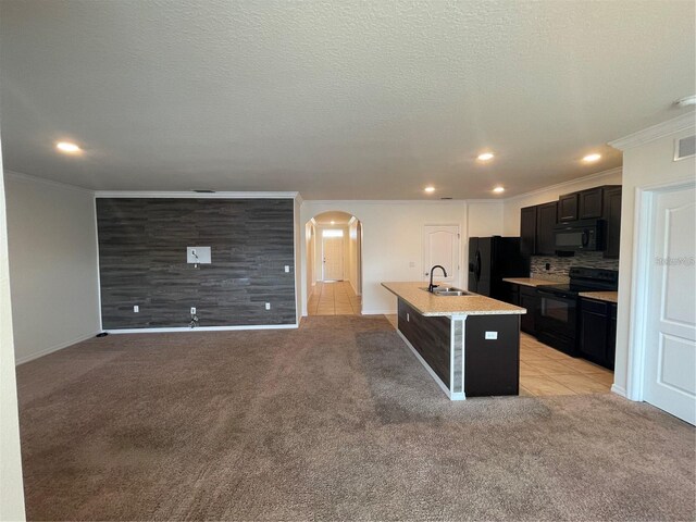 kitchen with an island with sink, black appliances, sink, and light carpet