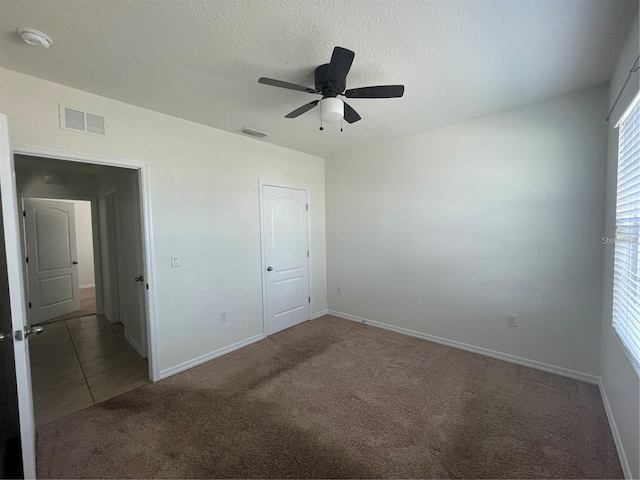 unfurnished bedroom with ceiling fan, a textured ceiling, a closet, and dark carpet