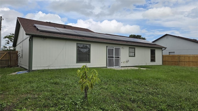 back of property with solar panels and a yard