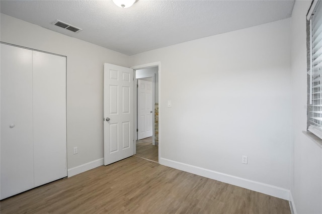 unfurnished bedroom featuring a textured ceiling, light wood-type flooring, and a closet