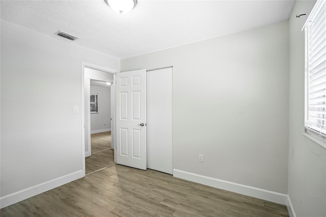 unfurnished bedroom with wood-type flooring, a closet, and a textured ceiling