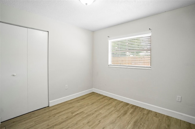 unfurnished bedroom featuring light wood-type flooring, a textured ceiling, and a closet