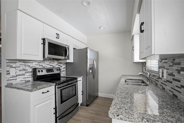 kitchen featuring white cabinets, light stone countertops, stainless steel appliances, light wood-type flooring, and sink