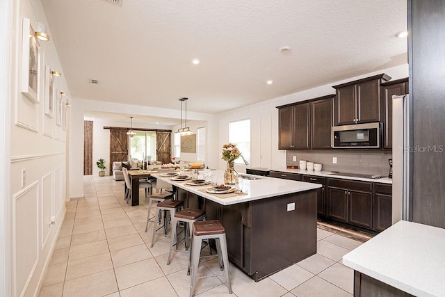 kitchen featuring a center island, backsplash, a kitchen breakfast bar, light tile patterned floors, and dark brown cabinetry