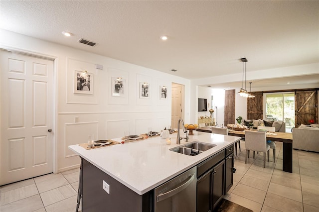 kitchen featuring dishwasher, sink, hanging light fixtures, an island with sink, and light tile patterned floors