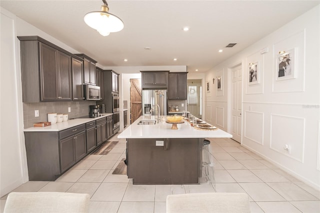 kitchen featuring a breakfast bar, sink, decorative backsplash, an island with sink, and stainless steel appliances