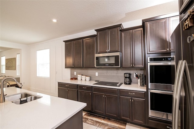 kitchen with tasteful backsplash, dark brown cabinetry, stainless steel appliances, sink, and light hardwood / wood-style flooring