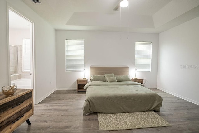 bedroom with a raised ceiling, ensuite bathroom, hardwood / wood-style floors, and ceiling fan