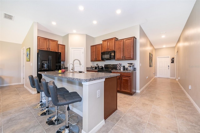 kitchen featuring light tile patterned flooring, an island with sink, sink, black appliances, and a kitchen breakfast bar