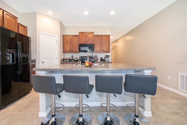 kitchen featuring an island with sink, black appliances, a kitchen bar, and light tile patterned flooring