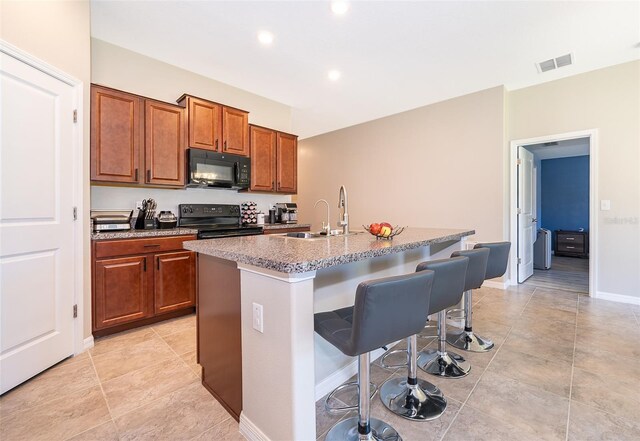 kitchen with a kitchen breakfast bar, black appliances, a kitchen island with sink, and sink