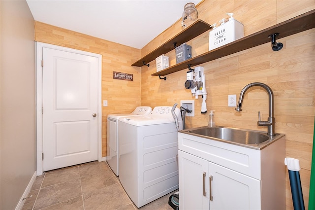 washroom with cabinets, wood walls, sink, and washing machine and dryer