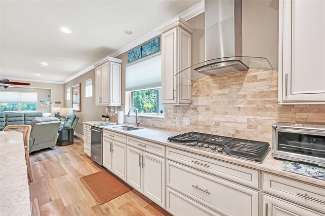 kitchen with ceiling fan, sink, wall chimney exhaust hood, appliances with stainless steel finishes, and light wood-type flooring