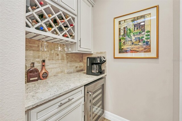 bar with tasteful backsplash, white cabinets, wine cooler, and light stone counters