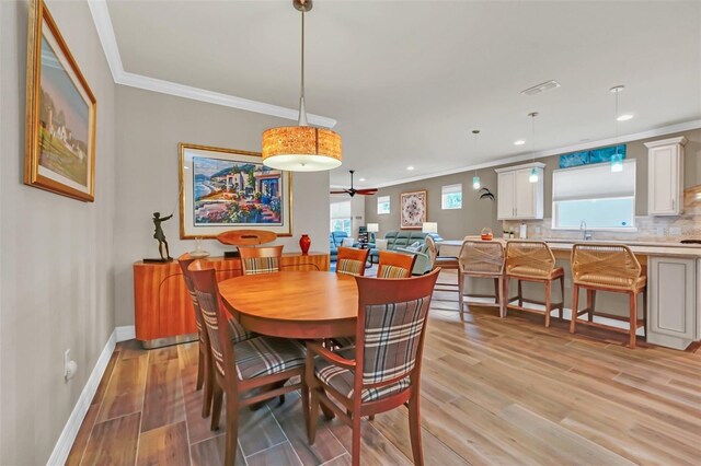 dining space with light wood-type flooring, ornamental molding, sink, and ceiling fan