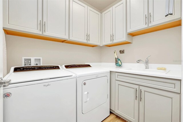 washroom featuring cabinets, light wood-type flooring, washing machine and clothes dryer, and sink