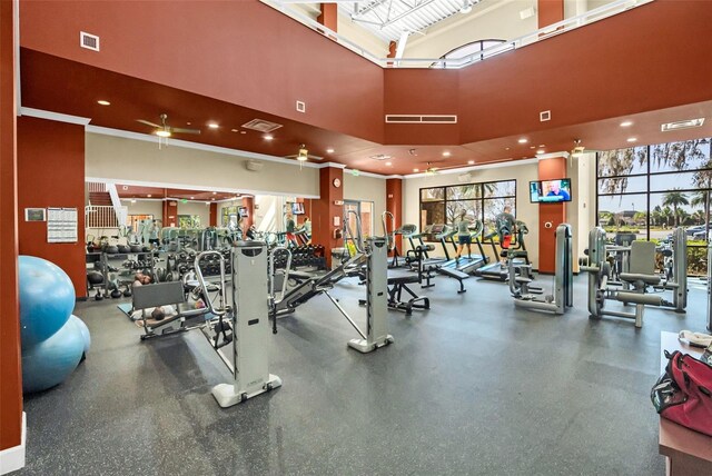 gym featuring a towering ceiling, ceiling fan, and crown molding