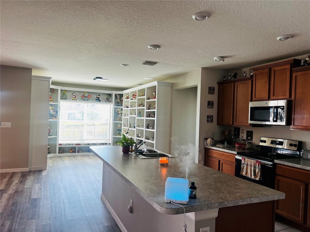 kitchen with hardwood / wood-style flooring, stainless steel appliances, a kitchen island with sink, and a textured ceiling