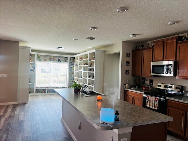 kitchen with hardwood / wood-style flooring, stainless steel appliances, a kitchen island with sink, and a textured ceiling