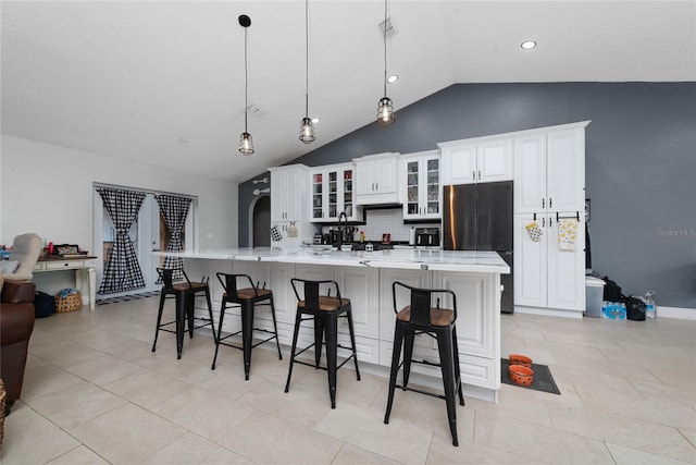 kitchen with a large island with sink, white cabinetry, stainless steel refrigerator, pendant lighting, and lofted ceiling