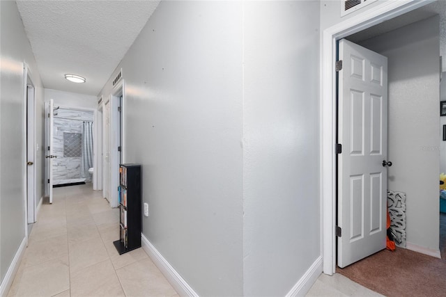 hall with a textured ceiling and light tile patterned floors